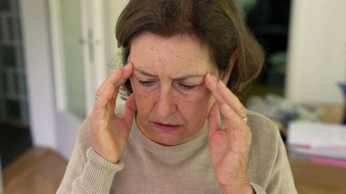 Olgun bir kadın yoğun bir baş ağrısı ya da stres yaşıyor, iki eliyle başını tutuyor, rahatsızlık ve endişelerini dile getiriyor. Yüz kırışıklıkları ve konsantrasyon, fiziksel ya da duygusal acı