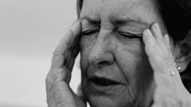 Yaşlı kadın yakın plan, gözleri kapalı, iki eli şakaklarına bastırıyor, derin kırışıklıklar ve acı dolu ifade, şiddetli stres ya da baş ağrısı