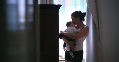 Anne bebeğini hafifçe aydınlatılmış bir odada kucağında tutuyor, bebeği huzurlu, şefkatli bir şekilde kucaklıyor ve onunla bağlantı kuruyor, sevgisini ve sakinliğini gösteriyor.