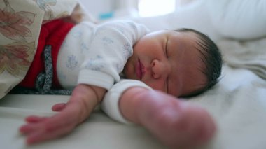 Yeni doğmuş bebek, kollarını uzatarak mışıl mışıl uyuyor. Rahatlamış ve huzurlu bir yüz ifadesi sergiliyor.