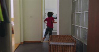 Çocuk bir evin koridorunda koşuyor, neşeli bir enerji ve hareket anı yakalıyor, çocukluğun kaygısız ruhunu ve neşesini aile ortamında gösteriyor.