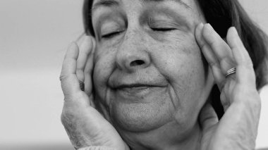 Yaşlı kadın yakın plan, gözleri kapalı, iki eli şakaklarına bastırıyor, derin kırışıklıklar ve acı dolu ifade, şiddetli stres ya da baş ağrısı