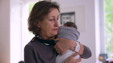 Anneanne yeni doğmuş bir bebeği omuzunda tutuyor, sakin bir yansıma anını yakalıyor ve kapalı bir ortamda aşkı yakalıyor.