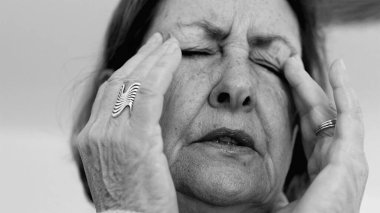 Yaşlı kadın yakın plan, gözleri kapalı, iki eli şakaklarına bastırıyor, derin kırışıklıklar ve acı dolu ifade, şiddetli stres ya da baş ağrısı