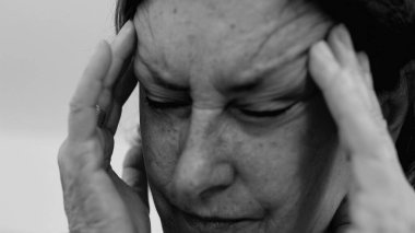 Yaşlı kadın yakın plan, gözleri kapalı, iki eli şakaklarına bastırıyor, derin kırışıklıklar ve acı dolu ifade, şiddetli stres ya da baş ağrısı