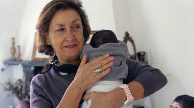 Büyükannem yeni doğmuş bir bebeği omzunda tutuyor, bebeği nazikçe okşuyor ve rahatlatıyor, şefkatli ve samimi bir sevgi ve ilgi anı yakalıyor.