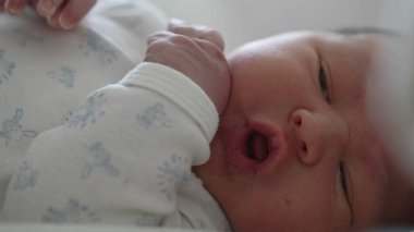 Yeni doğmuş bebek yatakta yatıyor, gözleri sonuna kadar açık, merakla etrafı keşfediyor. Bebek yüzü merak ve ilgi gösteriyor, doğal, yumuşak ışık içeride.