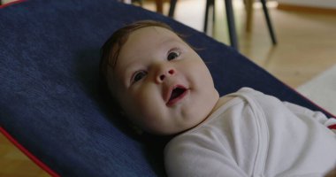 Bebek bir fedaide yatıyor, gülümsüyor ve mutlu görünüyor, rahat bir ev ortamında bir anlık mutluluğun ve konforun tadını çıkarıyor, erken çocukluğun neşesini ve masumiyetini vurguluyor.