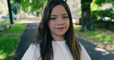 Parktaki ağaçlarla kaplı bir sokakta güler yüzlü bir kız, parlak bir günün tadını çıkarıyor, beyaz bir bluz ve desenli bir etek giyiyor, yemyeşil ile çevrili.