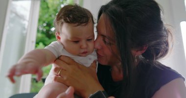 Anne sevgiyle bebeğini kucağında tutuyor, alınları birbirine değiyor, samimi ve duygusal bir bağ kurma anını paylaşıyor, sıcak bir yuva ortamında derin bir sevgi ve bağlantı kuruyor.