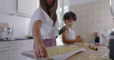 Çocuklar mutfakta hamur hazırlıyor, kız odaklanıyor, oğlan asistanı, aile yemekleri aktivitesi, anne arka planda, parlak ev dekorasyonu, etkileşimli öğrenme anı, takım çalışması