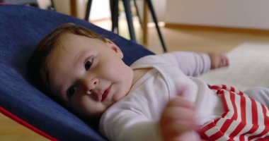 Bebek bir fedaide uzanıyor, sakince yukarı bakıyor, rahat bir ev ortamında rahatlığın ve rahatlığın tadını çıkarıyor, çocukluk yıllarının masumiyetini ve huzurunu gösteriyor.