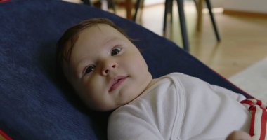 Bebek bir fedaide yatıyor, gülümsüyor ve mutlu görünüyor, rahat bir ev ortamında bir anlık mutluluğun ve konforun tadını çıkarıyor, erken çocukluğun neşesini ve masumiyetini vurguluyor.