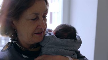 Anneanne yeni doğmuş bir bebeği omzuna yakın tutuyor, huzurlu bir ifadeyle, sevgi ve bağın hassas bir anını yakalıyor.