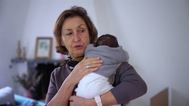 Büyükannem yeni doğmuş bir bebeği omzunda tutuyor, bebeği nazikçe okşuyor ve rahatlatıyor, şefkatli ve samimi bir sevgi ve ilgi anı yakalıyor.