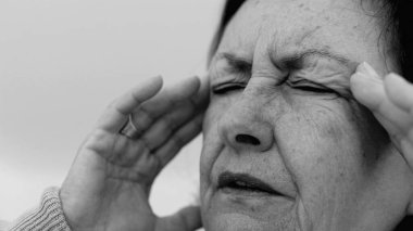 Yaşlı kadın yakın plan, gözleri kapalı, iki eli şakaklarına bastırıyor, derin kırışıklıklar ve acı dolu ifade, şiddetli stres ya da baş ağrısı
