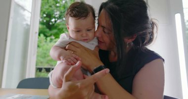 Anne sevgiyle bebeğini kucağında tutuyor, alınları birbirine değiyor, samimi ve duygusal bir bağ kurma anını paylaşıyor, sıcak bir yuva ortamında derin bir sevgi ve bağlantı kuruyor.