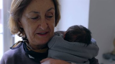 Anneanne yeni doğmuş bir bebeği omzuna yakın tutuyor, huzurlu bir ifadeyle, sevgi ve bağın hassas bir anını yakalıyor.