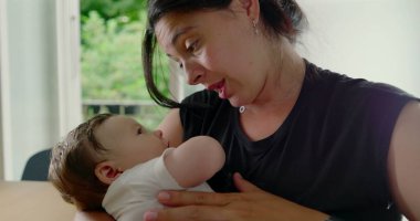 Anne ve bebek sevgi dolu bir anın tadını çıkarıyorlar. Bebek rahatça kollarına yerleşmiş sıcak, rahat bir ev ortamında aralarındaki bağ ve sevgiyi vurguluyor.