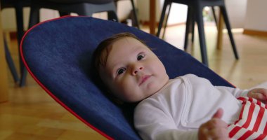 Bebek bir fedaide uzanıyor, sakince yukarı bakıyor, rahat bir ev ortamında rahatlığın ve rahatlığın tadını çıkarıyor, çocukluk yıllarının masumiyetini ve huzurunu gösteriyor.