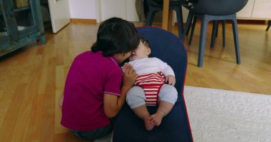 Büyük kardeş, bir fedainin içindeki küçük kardeşle etkileşime girmek için eğiliyor, aralarında hassas ve sevgi dolu bir anı vurguluyor, bir yuva ortamında çocukluğun masumiyetini ve neşesini yakalıyor.