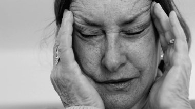 Yaşlı kadın yakın plan, gözleri kapalı, iki eli şakaklarına bastırıyor, derin kırışıklıklar ve acı dolu ifade, şiddetli stres ya da baş ağrısı