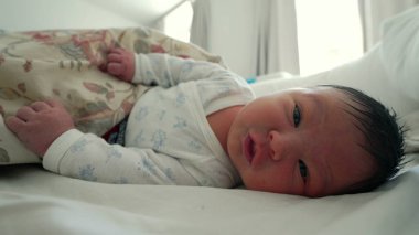 Çiçekli bir battaniyenin altında dinlenen yeni doğmuş bebek, çevresini keşfederken yüzünü buruşturuyor ve işaret ediyor, hayatın ilk ayı ve erken gelişim kilometre taşları.