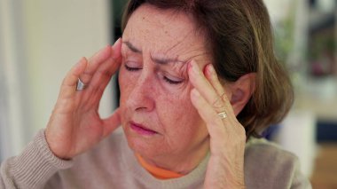 Şiddetli baş ağrısı çeken bir kadın, gergin bir ifadeyle parmaklarını şakaklarına bastırıyor. Kapalı gözler, çatık kaşlar, derin konsantrasyon ve belirgin zihinsel gerginlik, duygusal acı.
