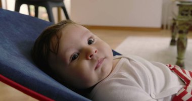 Bebek bir fedaide yatar, düşünceli bakar ve görünür, rahat bir ev ortamında bir anlık sakinlik ve yansıma yakalar, çocukluk zamanının masumiyetini ve huzurunu gösterir.