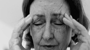 Yaşlı kadın yakın plan, gözleri kapalı, iki eli şakaklarına bastırıyor, derin kırışıklıklar ve acı dolu ifade, şiddetli stres ya da baş ağrısı