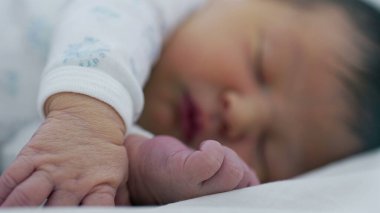 Yeni doğan bebek el ve ayakla uyuyor. Bebeklik döneminin hassas ve nazik doğasını vurguluyor.