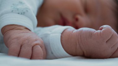 Bebek arka planda huzur içinde uyurken, yeni doğmuş bir bebeğin küçük yumruklarının yakın çekimi.