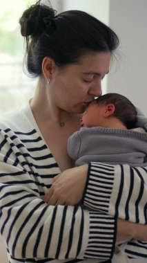 Anne yeni doğmuş bebeğini göğsüne yakın tutuyor, şefkatli bir ifadeyle aşağıya bakıyor. Anne ile çocuk arasındaki güçlü bağ sakin ve kapalı bir ortamda