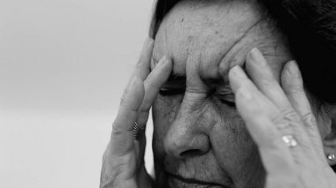 Yaşlı kadın yakın plan, gözleri kapalı, iki eli şakaklarına bastırıyor, derin kırışıklıklar ve acı dolu ifade, şiddetli stres ya da baş ağrısı