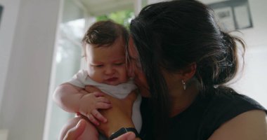 Anne sevgiyle bebeğini kucağında tutuyor, alınları birbirine değiyor, samimi ve duygusal bir bağ kurma anını paylaşıyor, sıcak bir yuva ortamında derin bir sevgi ve bağlantı kuruyor.