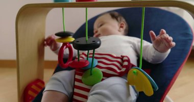 Bebek, bir fedainin içinde yatarken oyuncaklarla oynuyor, rahat bir ev ortamında merak ve neşe dolu bir an sergiliyor, çocukluk yıllarının masumiyetini ve neşesini vurguluyor.