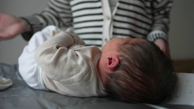 Anne yeni doğmuş bir bebeği nazikçe değişen bir paspasın üzerine yerleştirir, giysiyi özenle ayarlar. Bebekler annelerine bakar. Bir anlık bir yakınlık ve şefkat gösterirler.