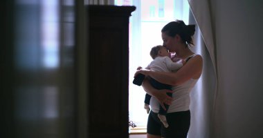 Anne bebeğini hafifçe aydınlatılmış bir odada kucağında tutuyor, bebeği huzurlu, şefkatli bir şekilde kucaklıyor ve onunla bağlantı kuruyor, sevgisini ve sakinliğini gösteriyor.