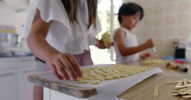 Kız ve erkek mutfakta para kazanıyor, anne arka planda, çocuklar aşçılık faaliyetinde, aile çalışması, parlak ev ortamı, etkileşimli yemek pişirme anı