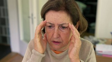 Olgun bir kadın yoğun bir baş ağrısı ya da stres yaşıyor, iki eliyle başını tutuyor, rahatsızlık ve endişelerini dile getiriyor. Yüz kırışıklıkları ve konsantrasyon, fiziksel ya da duygusal acı