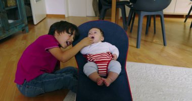 Büyük kardeş, bir fedainin içindeki küçük kardeşle etkileşime girmek için eğiliyor, aralarında hassas ve sevgi dolu bir anı vurguluyor, bir yuva ortamında çocukluğun masumiyetini ve neşesini yakalıyor.