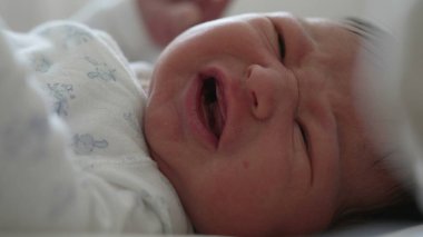 Yeni doğmuş bebek yatakta yatıyor, gözleri sonuna kadar açık, merakla etrafı keşfediyor. Bebek yüzü merak ve ilgi gösteriyor, doğal, yumuşak ışık içeride.