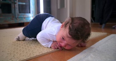 Ağlayan bebek yerde yatıyor, sıkıntı ve rahatsızlık gösteriyor, ev ortamında yumuşak bir paspas üzerinde duygularını ifade ediyor, erken gelişim zorluklarını ve hislerini vurguluyor.