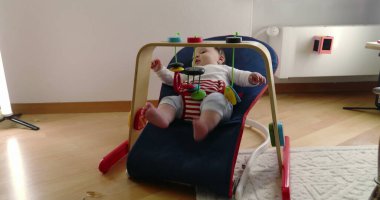 Bebek, bir fedainin içinde yatarken oyuncaklarla oynuyor, rahat bir ev ortamında merak ve neşe dolu bir an sergiliyor, çocukluk yıllarının masumiyetini ve neşesini vurguluyor.