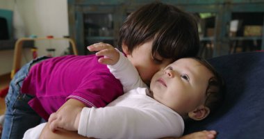 Büyük kardeş, bir fedainin üzerindeki küçük kardeşle şefkatle iletişim kuruyor. Bir yuva ortamında aralarındaki güçlü bağı ve sevgiyi vurgulayan dokunaklı ve sevgi dolu bir an yaratıyor.