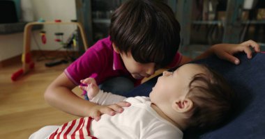 Ağabeyi, bir fedainin üzerine uzanmış küçük kardeşini alnından nazikçe öpüyor, hassas ve sevgi dolu bir anı yakalıyor ve yuva ortamındaki güçlü bağlarını vurguluyor.