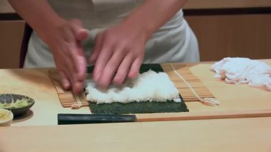 Deniz yosunlarının üzerine suşi pilavı sermek, el hareketleri, geleneksel suşi yapma süreci, Japon mutfağı hazırlığı, bambu hasırı, aşçılık sanatındaki detaylara dikkat etmek.