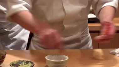 Suşi şefi karidesi nazikçe tutuyor, yakın plan, otantik Japon mutfağında titiz ve geleneksel hazırlık, sakin odaklanma ve rafine mutfak tekniği