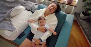 Anne, bebek göğsünde tutarken gözleri kapalı dinleniyor. Aydınlık ve rahat bir ev ortamında kanepede sakin ve huzurlu bir anın tadını çıkarıyor.