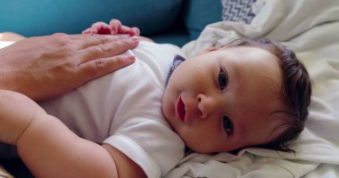 Bebek koltukta uzanıyor, yumuşak ışıklandırma ve besleyici bir atmosferle dolu sıcak ve huzurlu bir ev ortamında bir el tarafından nazikçe teselli ediliyor.